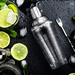 Cocktail shaker with lime slices and ice on a dark surface