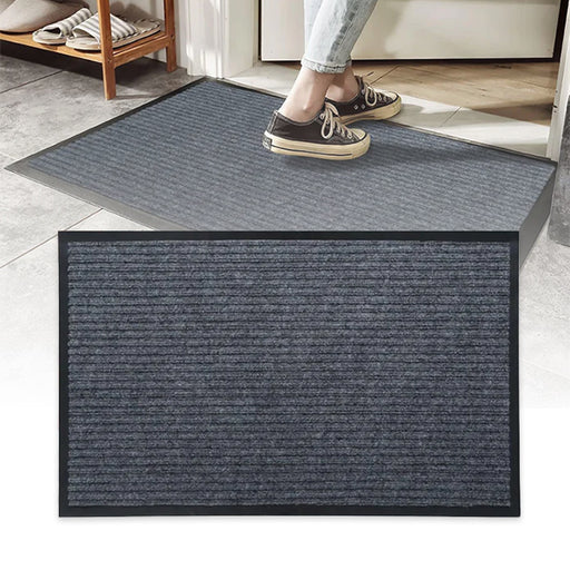 Indoor outdoor door mat with non-slip rubber backing, shown in gray with a textured surface, placed on the floor and a person stepping on it.
