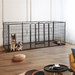Black metal pet playpen with two dogs inside in a room with wooden flooring and furniture.