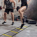 Person using a agility ladder with another person lifting weights in the background.