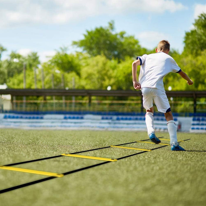 Person using a yellow agility ladder on a sports field with trees in the background