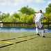 Person using a yellow agility ladder on a sports field with trees in the background
