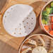 White steamer basket with gold dots on a wooden surface with vegetables and dumplings.
