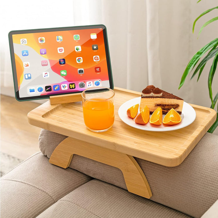 Wooden lap desk on a couch with a tablet, juice, and cake.