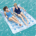 Two women lying on an inflatable pool raft with blue bottles on a pool.