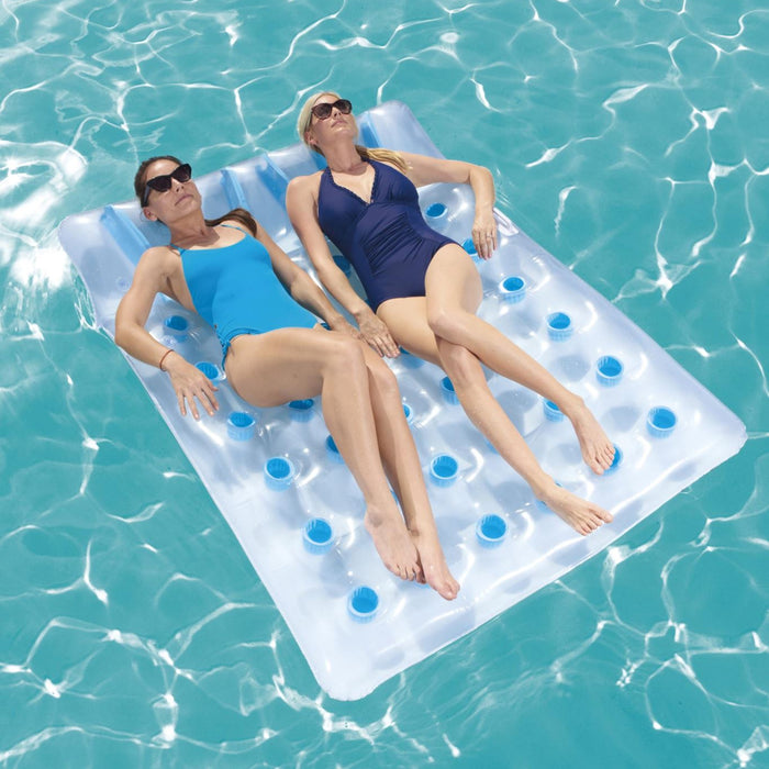 Two people lying on an inflatable pool float with blue floats in clear blue water.