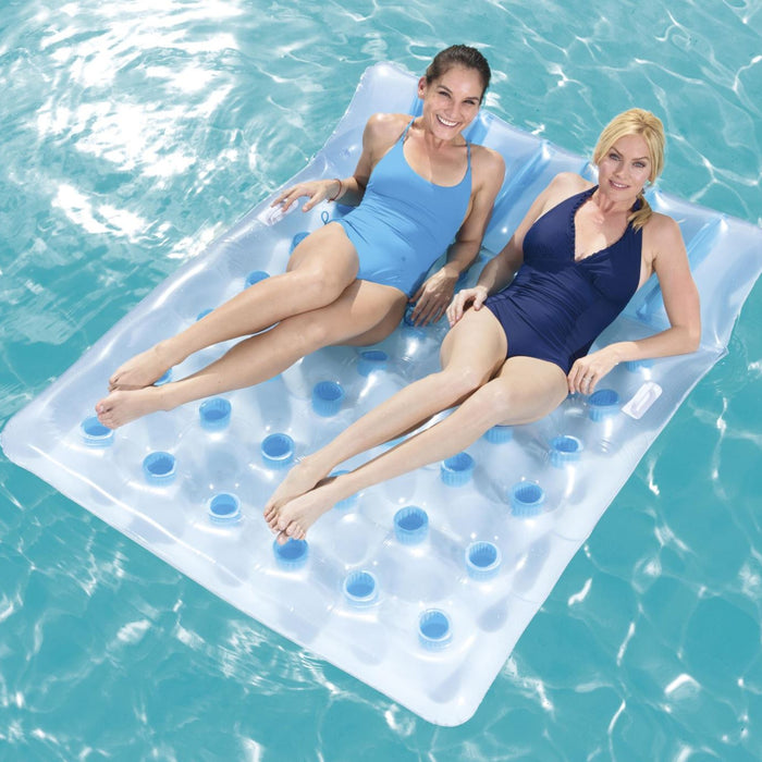 Two women relaxing on a large inflatable pool raft in clear blue water.
