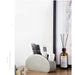 White remote control holder with remotes on a wooden surface next to a bottle of diffuser.