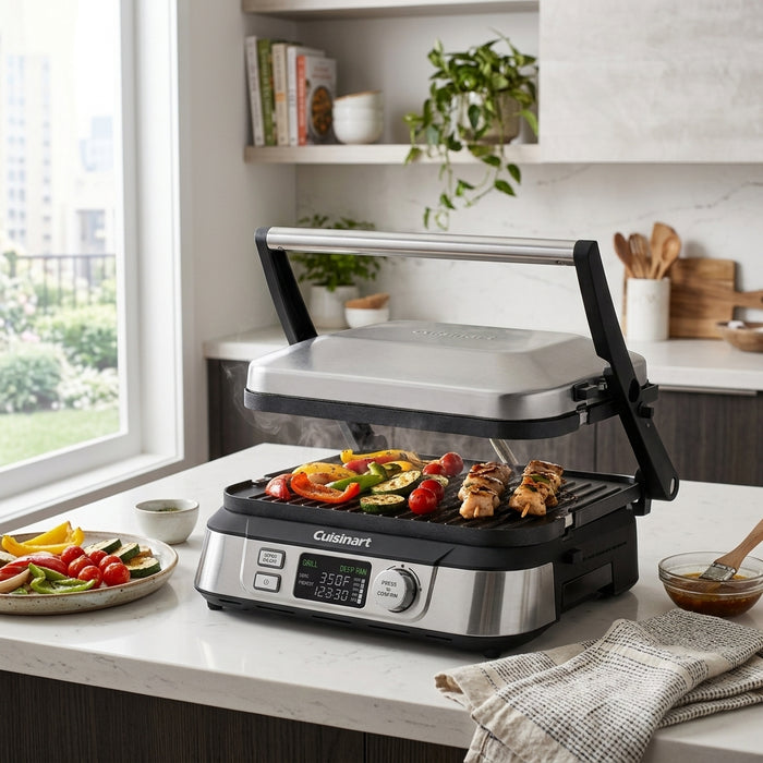 Cuisinart indoor electric grill sizzling with food on a marble countertop in a bright, modern kitchen.