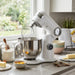 A white Cuisinart Precision Pro Digital Stand Mixer on a granite kitchen countertop surrounded by baking ingredients like flour, eggs, and butter.