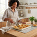 A woman in an apron stands at a kitchen island, using wooden tongs to serve a single golden-brown galette from a full baking sheet.