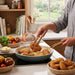 A person is using wooden tongs to flip fried chicken in a smokey bluecpan.