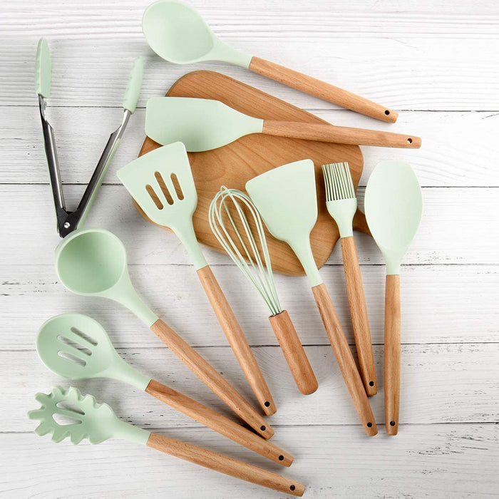 Set of kitchen utensils with green handles and wooden shafts on a white wooden surface.