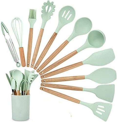 Set of green kitchen utensils with wooden handles in a holder on a white background