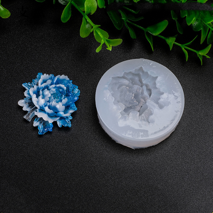 Blue flower silicone mold on a black surface with green leaves in the background