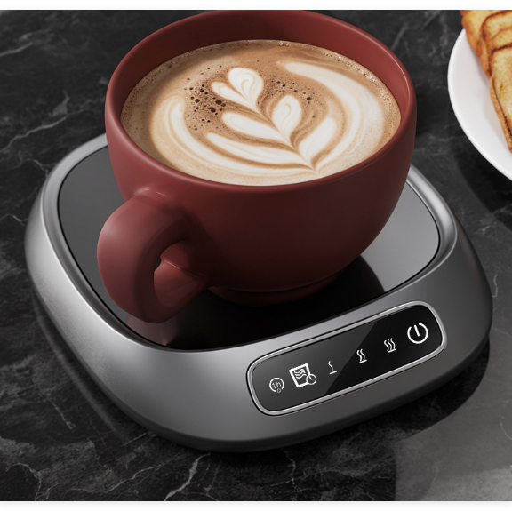 Red mug with latte art on a black marble surface with a hot beverage warmer.