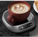 Red mug with latte art on a black marble surface with a hot beverage warmer.