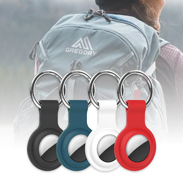 Four silicone AirTag case keychains in black, white, blue, and red, attached to a metal carabiner, displayed in front of a person wearing a backpack.