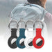 Four silicone AirTag case keychains in black, white, blue, and red, attached to a metal carabiner, displayed in front of a person wearing a backpack.