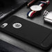 A black textured phone case with a carbon-fiber pattern accent on the corners, shown on an iPhone. The case is photographed in a styled flat-lay setting alongside a leather wallet, a wristwatch with a red, white, and navy strap, and a silver metal flask.
