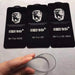 Three black cards with 9H branding and text, held by a hand with a clear object in front of them on a light gray background.