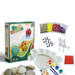A rock painting kit which includes various paints, brushes, glitter, and decorative stickers displayed alongside smooth stones, all packaged in a colorful box.