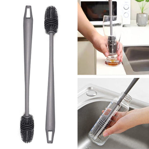 A set of two long handle silicone bottle brushes, one standing upright and the other lying horizontally, displayed alongside a glass of water and a sink.