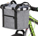 A gray bike storage basket with a woven canvas construction, attached to a bicycle handlebar. The basket has black straps and a silver aluminum frame.