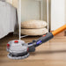A product image shows a gray and clear motorized mop head attachment on an orange stick vacuum pole, cleaning a wooden floor near a bed. The low-profile design with two spinning pads and red accents is visible, emphasizing its ability to clean under furniture.