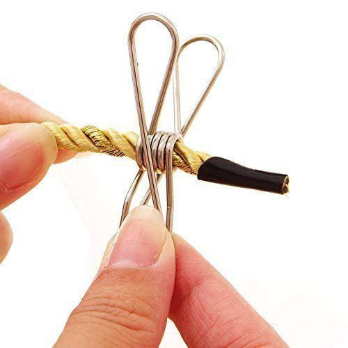 
A close-up shot of a hand using a single stainless steel spring-loaded mini clothes peg to clamp a section of twisted gold and brown rope. The finger and thumb of the hand are visible, holding the peg open around the rope. One end of the rope has a black, capped tip.