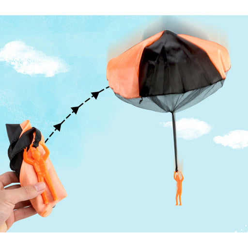 A hand holding a black and orange toy parachute which appears to be designed to be thrown as a flying toy.