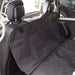 A close-up photo of a black, quilted, waterproof pet hammock/car seat cover installed on the rear bench seat of a vehicle. The cover is secured around the headrests with adjustable straps and protects the backrest and bench seat.