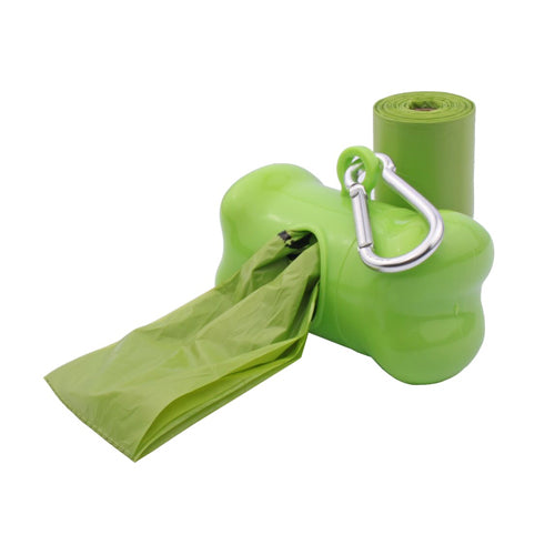 A bright green, bone-shaped pet waste bag dispenser with a silver carabiner clip, shown with a matching green bag and refill roll. A green waste bag is being pulled out of the dispenser opening, and a new roll of green bags is visible standing behind it.