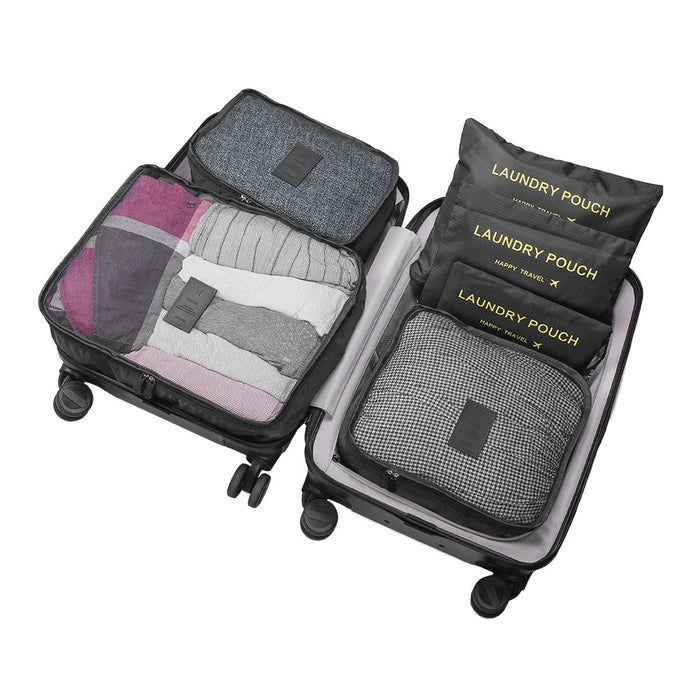 An open black rolling suitcase is efficiently organized with a set of travel packing cubes and laundry pouches. The cubes are packed with folded clothing and the right side holds three stacked black flat laundry pouches and a large patterned cube, showcasing a complete luggage organizer system.
