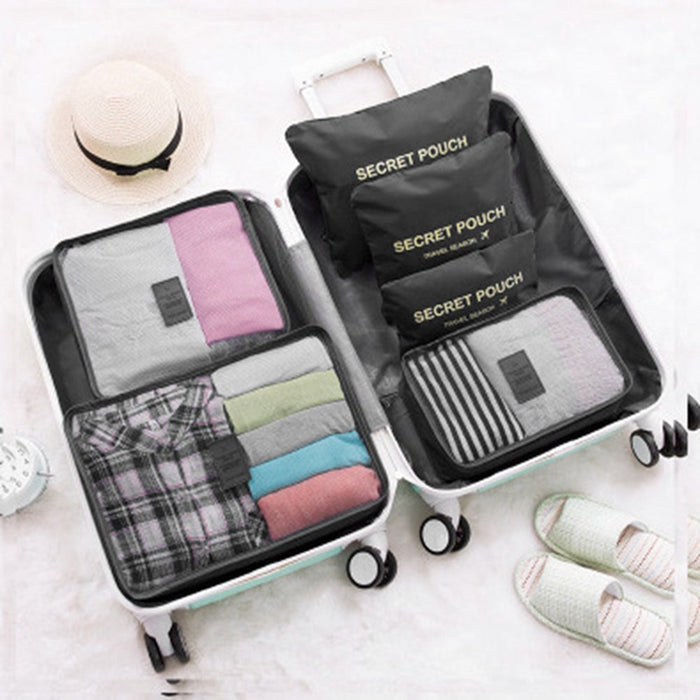 An open suitcase is organized with travel packing cubes and pouches. The suitcase contains mesh-top cubes holding folded and rolled clothing, along with three stacked black "SECRET POUCH" bags. A straw hat and slippers are nearby.