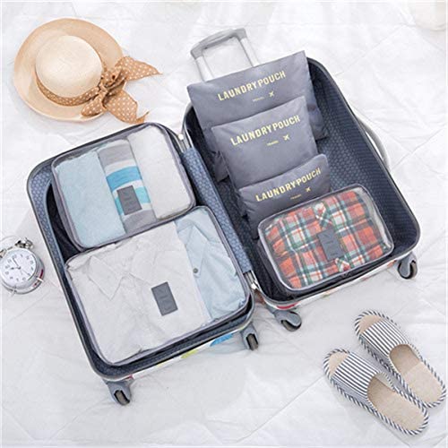 An open rolling suitcase is neatly organized with light gray travel packing cubes and laundry pouches. The left side contains mesh-top cubes with folded clothes, while the right side has three stacked "LAUNDRY POUCH" bags and a patterned cube. A straw hat and slippers are visible nearby.