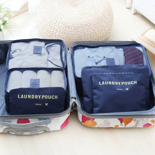 An open, patterned suitcase is neatly organized using **dark blue travel packing cubes** and a **mesh laundry pouch**. The cubes store folded shirts and rolled garments, demonstrating an effective **travel organizer** system. A large, woven ottoman is visible in the background.