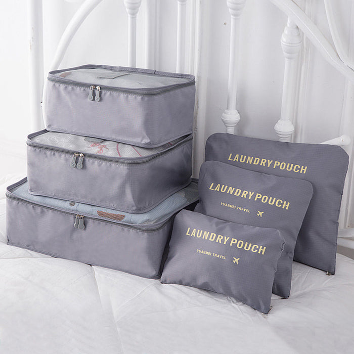 A set of three stacked light gray mesh-top packing cubes and three matching flat "LAUNDRY POUCH" bags, all with gold labeling, are displayed together on a white bedspread, showcasing a complete luggage organization set.