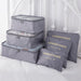 A set of three stacked light gray mesh-top packing cubes and three matching flat "LAUNDRY POUCH" bags, all with gold labeling, are displayed together on a white bedspread, showcasing a complete luggage organization set.